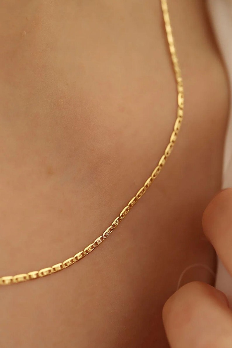 May include: A delicate gold chain necklace with a simple, classic design. The chain is made of small, oval-shaped links.