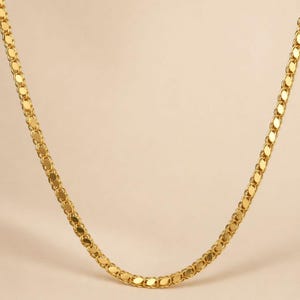 May include: A gold-colored necklace with a delicate, flat chain design. The chain is composed of small, interconnected oval links, creating a smooth, continuous appearance. The necklace is displayed against a neutral background.