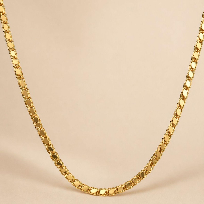May include: A gold-colored necklace with a delicate, flat chain design. The chain is composed of small, interconnected oval links, creating a smooth, continuous appearance. The necklace is displayed against a neutral background.