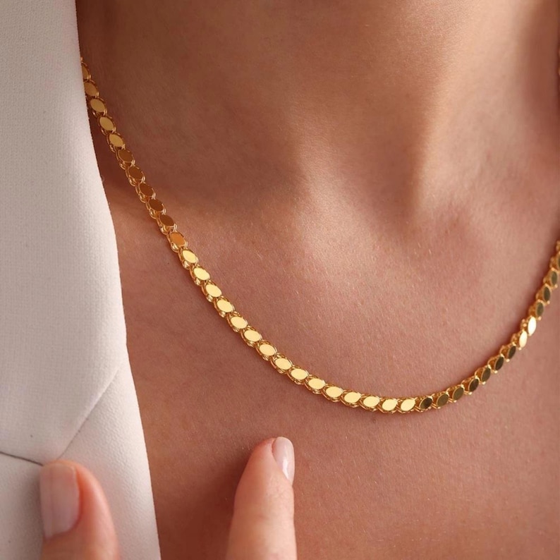 May include: A gold-colored necklace with a delicate, repeating teardrop design. The necklace is worn around the neck, and the image is a close-up, highlighting the jewelry's details and shine. The necklace is a fashion accessory.