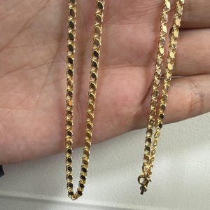 May include: A delicate gold necklace with a repeating oval link design. The chain is displayed against a neutral background, showcasing its bright, reflective surface. The necklace is a classic jewelry piece.