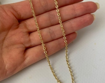 Puede incluir: Un delicado collar dorado con un diseño de cadena de eslabones ovalados repetidos. La cadena está finamente detallada, reflejando la luz. El collar se muestra sobre un fondo neutro. Una joya elegante.