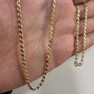May include: A gold-colored necklace with a delicate, repeating oval link design. The chain is displayed against a neutral background, showcasing its polished finish and intricate pattern. The necklace is a jewelry item.