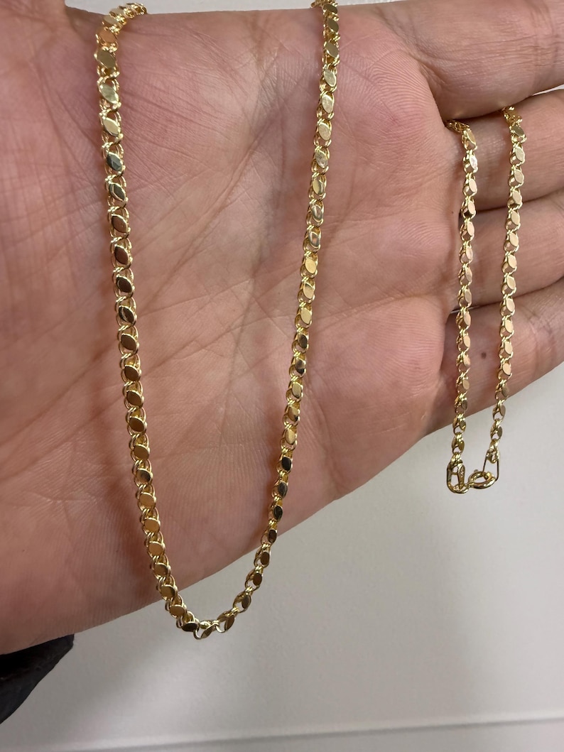 May include: A gold-colored necklace with a delicate, repeating oval link design. The chain is displayed against a neutral background, showcasing its polished finish and intricate pattern. The necklace is a jewelry item.