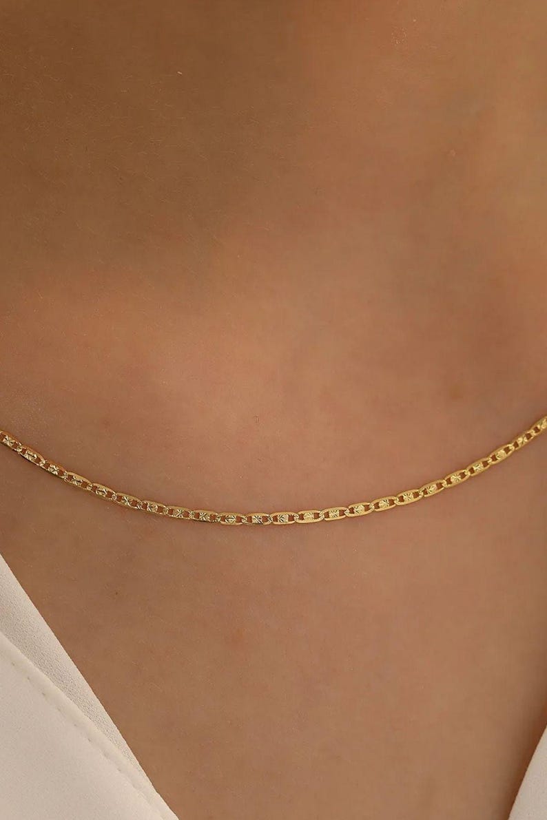 May include: A delicate gold chain necklace with a simple, classic design. The chain is made of small, linked oval shapes.