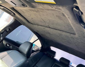 May include: The interior of a vehicle featuring a dark gray suede headliner, a sunroof panel, black leather seats, and a black seatbelt buckle with the Infiniti logo visible on the rear seat assembly near the center console area.