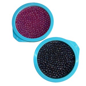 Puede incluir: Dos cepillos redondos para el cabello, de color turquesa. Uno tiene un interior morado oscuro lleno de pequeñas cuentas transparentes. El otro tiene un interior negro con cuentas similares. Cada cepillo tiene un pequeño mango en el lateral.