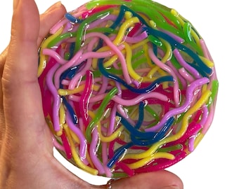 May include: A round, colorful resin coaster filled with vibrant, squiggly, worm-like shapes. The coaster features a mix of bright colors, including pink, yellow, green, blue, and purple. The coaster is held in a hand against a white background.
