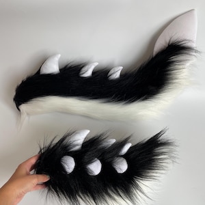 Könnte beinhalten: Ein schwarz-weißes Kunstfell-Schwanz- und Pfoten-Set. Der Schwanz ist lang und hat eine weiße Spitze. Die Pfote hat weiße Krallen. Das Set ist für Kostüm- oder Cosplay-Zwecke konzipiert.