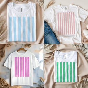 Puede incluir: Cuatro camisetas blancas con dise&ntilde;os de rayas verticales en azul, rosa, morado y verde. Las camisas se muestran sobre un fondo neutro con elementos decorativos. Las camisetas son de manga corta y tienen cuello redondo.