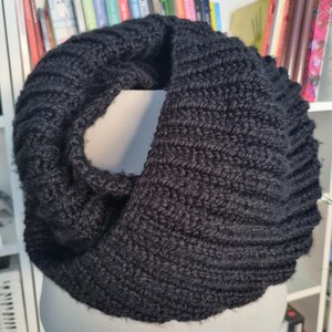 May include: A black knitted infinity scarf with a textured pattern. The scarf is folded in half and draped over a mannequin.