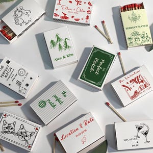 Puede incluir: Una colecci&oacute;n de cajas de cerillas decorativas con varios dise&ntilde;os y texto. Algunas cajas presentan ilustraciones de gatos, c&oacute;cteles y gr&aacute;ficos tem&aacute;ticos de bodas. El texto incluye nombres, fechas y frases como "Perfect Match."