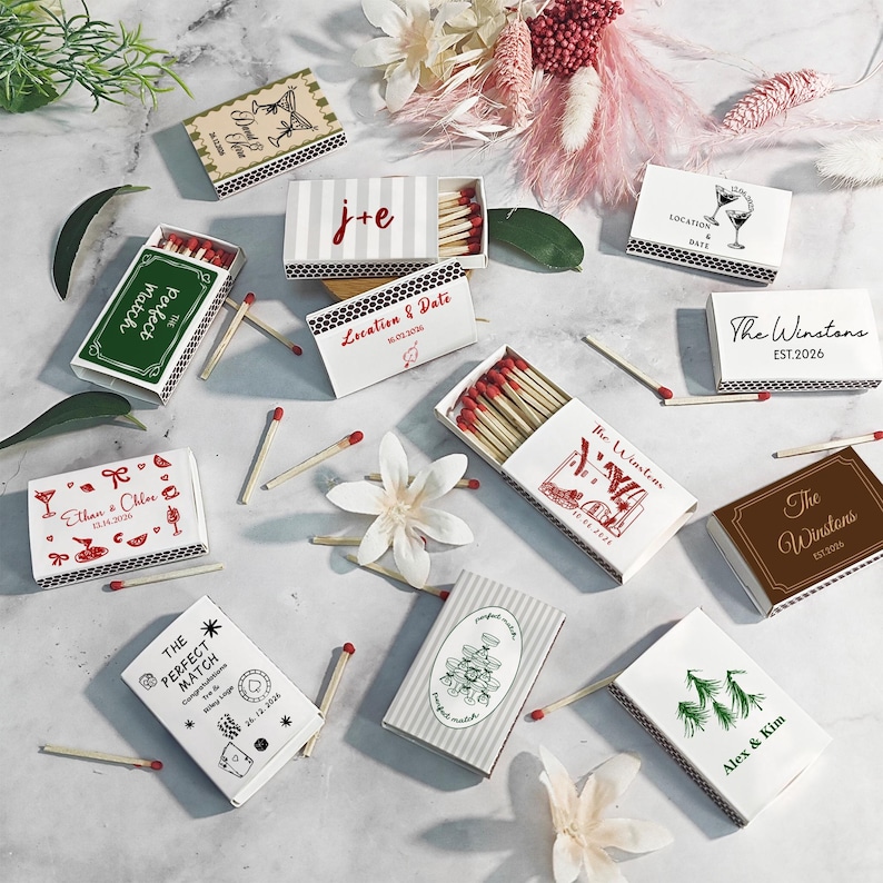 Puede incluir: Una variedad de cajas de cerillas decorativas con varios dise&ntilde;os y textos. Algunas cajas son blancas con detalles rojos, otras verdes o marrones. El texto incluye nombres, fechas y frases como "The Perfect Match."