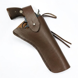 May include: A dark brown leather holster containing a revolver with a dark metal frame and textured wooden grips. The holster features a single silver-coloured metal snap closure on the strap and a long leather cord extending from the side.