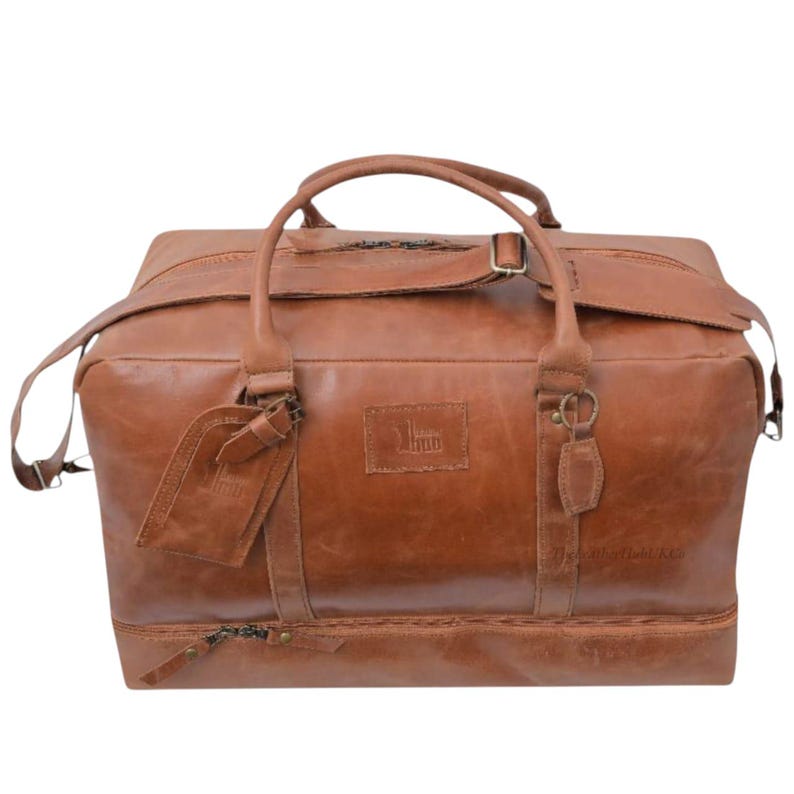 May include: A brown leather duffel bag with a top handle, shoulder strap, and a luggage tag. The bag has a rectangular shape with a zipper closure and a small embossed logo. The leather has a distressed look.