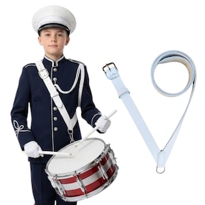Può includere: Una persona in uniforme da banda blu navy con cappello e guanti bianchi, che tiene le bacchette sopra un tamburo rosso e argento. Una tracolla per tamburo in pelle bianca è mostrata separatamente. L'uniforme ha dettagli bianchi.