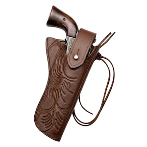 May include: A brown leather holster featuring an embossed floral pattern and a secure strap with a silver-toned metal snap button. The holster contains a revolver with a dark wooden grip and intricate metal engravings on the frame and cylinder.