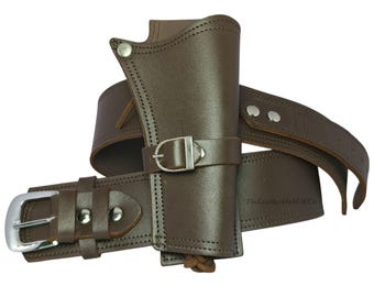 May include: Brown leather holster and belt set. The holster is designed to hold a handgun and is attached to a wide belt with a silver buckle. The set is made of brown leather and features silver rivets and a silver buckle.