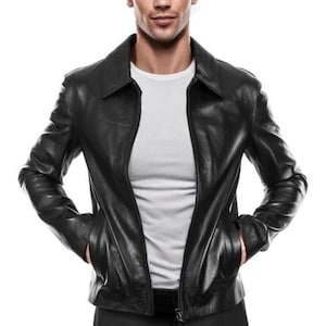 Könnte beinhalten: Schwarze Lederjacke mit Kragen und Reißverschluss. Die Jacke hat zwei Vordertaschen und wird über einem weißen T-Shirt getragen. Das Design ist klassisch und zeitlos, passend für verschiedene Anlässe.
