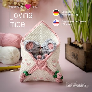 Può includere: Una busta all'uncinetto fatta a mano con due topi grigi all'interno, accentuata con filato rosa e bianco. La busta è decorata con un cuore rosa e rose. Il testo sull'immagine recita "Loving mice" e "English crochet pattern US terms."