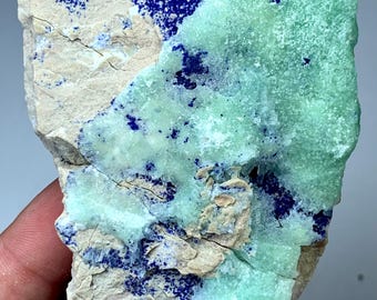 May include: A close-up of a mineral specimen featuring a combination of colors and textures. The rock displays areas of deep blue, light green, and beige, with a crystalline structure. The mineral is a natural formation.