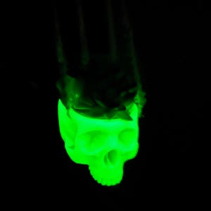 May include: A green glowing plastic skull with a black background.