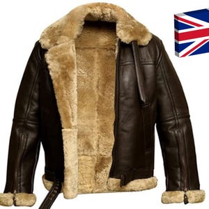 Può includere: Giacca in pelle marrone scuro con fodera e colletto in montone. La giacca, in classico stile aviatore, presenta chiusura con zip e dettagli con fibbia. L'immagine mostra la giacca su sfondo bianco, con una bandiera britannica.