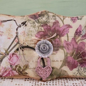 May include: A decorative wooden key holder with a floral design and a bicycle silhouette. It features four clear glass knobs and a heart-shaped charm. The text "W.I. TEXAS" is visible on the left side.