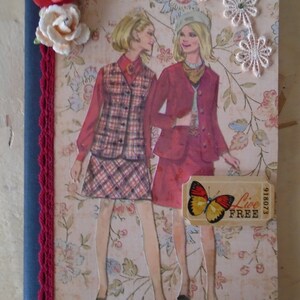 May include: A vintage-style scrapbook cover with two women in 1960s fashion. The women are wearing plaid and red dresses with white collars. The cover features a floral pattern, lace trim, and a butterfly sticker with the text "Live Free".