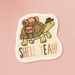 May include: A die-cut sticker featuring a cartoon turtle wearing a brown hat and carrying a pink sleeping bag and a small brown backpack on its shell. The text "SHELL YEAH!" is printed in brown and pink letters below the turtle illustration.