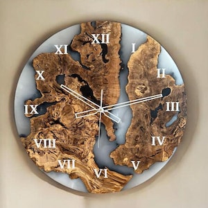Pode incluir: Um relógio de parede grande e redondo com numerais romanos. O mostrador do relógio é feito de madeira com um padrão natural de grão de madeira e um revestimento de resina epóxi transparente. Os ponteiros do relógio são prateados e o fundo é branco.