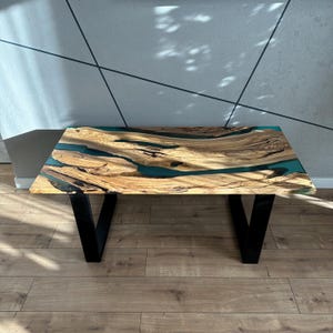 May include: A wooden coffee table with a teal epoxy resin inlay. The table has black metal legs.