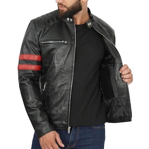 Op de afbeelding: Zwarte leren jas met rode strepen op de linkermouw. De jas heeft een ritssluiting, gewatteerde schouderdetails en een klein ritszakje op de borst. Het model draagt een zwart shirt en een blauwe jeans.