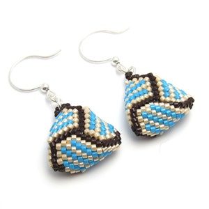 May include: A pair of earrings with a geometric design. The earrings are made of brown, blue, and cream colored beads. The earrings are hanging from silver hooks.