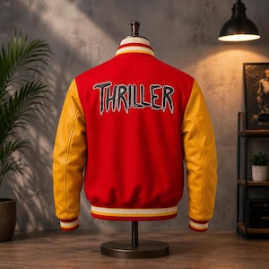May include: A red varsity jacket with yellow sleeves and ribbed cuffs. The back features the word THRILLER in large, black, stylised lettering with a white outline. The collar and hem have red, yellow, and white striped detailing.