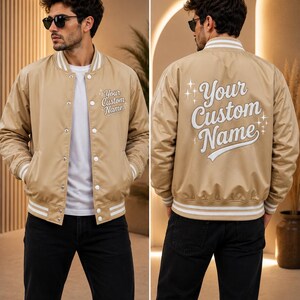 May include: A beige varsity jacket with white striped ribbed trim on the collar, cuffs, and hem. The front features the text Your Custom Name, and the back displays the same text in a larger font with decorative star accents on both sides.