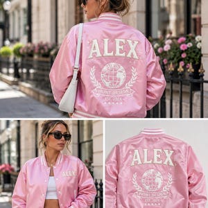 May include: A light pink satin bomber jacket featuring white striped ribbed trim at the collar, cuffs, and hem. The back displays white embroidered text reading ALEX, a globe graphic, and the words PRINT DESIGN EST. 2024 with five small stars.
