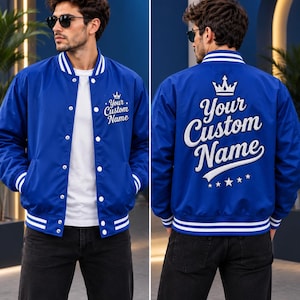 May include: A royal blue varsity jacket featuring white striped ribbed trim on the collar, cuffs, and hem. The front displays the text Your Custom Name with a crown icon. The back features the same text in large white script with a crown and stars.
