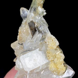 May include: A cluster of quartz crystals with a variety of colors and textures. The crystals are clear and translucent, with some areas showing a light yellow hue. There are also darker, almost black, inclusions within the quartz.