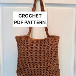 Puede incluir: Una bolsa de mano de crochet marrón con un asa de crochet colgada de una puerta blanca. El texto "CROCHET PDF PATTERN" está impreso en un rectángulo blanco.