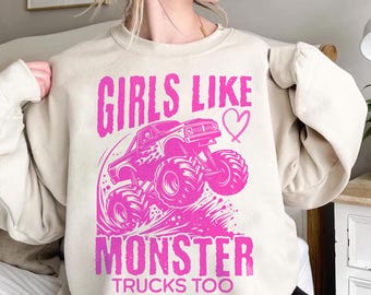 May include: A light beige sweatshirt with a pink graphic of a monster truck and the text "Girls Like Monster Trucks Too" with a pink heart.