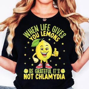 Può includere: Maglietta nera con un personaggio di cartone animato di limone giallo e il testo "When life gives you lemons be grateful it's not chlamydia."