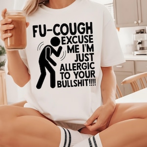 Pode incluir: Camiseta branca com um gráfico preto e texto que diz "FU-COUGH EXCUSE ME I'M JUST ALLERGIC TO YOUR BULLSHIT!!!!". Uma pessoa está segurando um copo de líquido marrom.