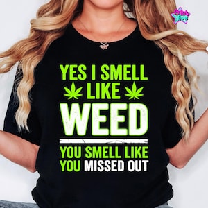 May include: Black t-shirt with the text "YES I SMELL LIKE WEED" in green and white, along with cannabis leaf graphics. The bottom of the shirt reads "YOU SMELL LIKE YOU MISSED OUT".