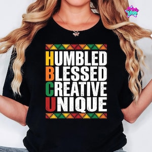 May include: Black t-shirt featuring the words "HUMBLED BLESSED CREATIVE UNIQUE" in white. The letters HBCU are in yellow, orange, green, and red. The design includes colourful geometric patterns at the top and bottom of the text.