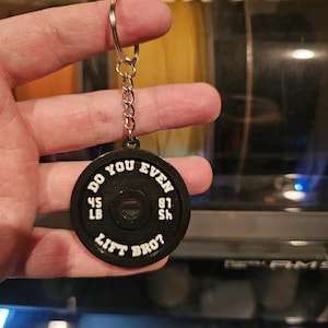 May include: Black weight plate keychain with white text that reads "Do you even lift bro?" with the weight measurements "45 lb" and "81 sh" on the plate.