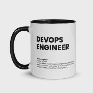 May include: White ceramic mug with a black handle and interior. The mug features the text "DEVOPS ENGINEER" in bold black letters. Below the text is a definition of DevOps Engineer.