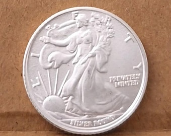 May include: A silver Walking Liberty half dollar coin. The coin features a woman walking towards the sun with the words "Silver Dollar" and "Privately Minted" inscribed on the coin.