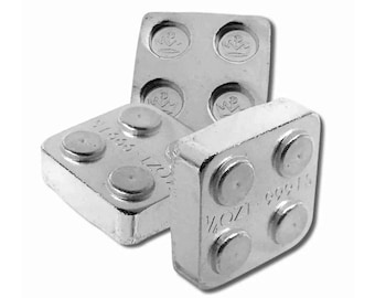 May include: Three silver bullion bars, each with four raised circular elements. The bars are stamped with "1/2 OZ" and "999.15" along with other text. The bars are arranged in a slightly overlapping manner against a white background.
