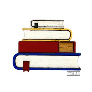 Pode incluir: Uma pilha de quatro livros de madeira com páginas brancas e capas coloridas. O livro superior é prateado, o segundo tem uma lombada dourada, o terceiro é vermelho e o livro inferior é azul. Uma fita de leitura vermelha é visível.